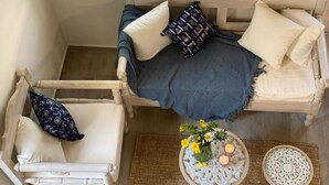 Een knus ingerichte kamer met een houten bank, twee fauteuils, een klein rond tafeltje met kaarsen en een decoratief bord.