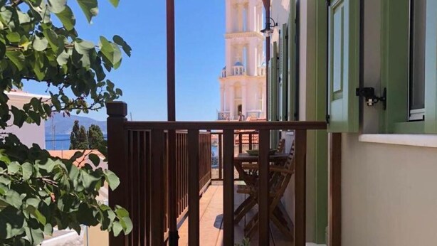 Een balkon met houten hekwerk, een beige parasol en uitzicht op een witte toren met balkons.