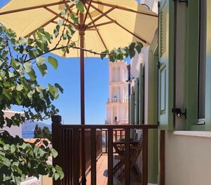 A balcony with a wooden railing, a beige umbrella, and a view of a white tower with balconies. - LUCA'S HOUSES-One Bedroom Apartment (XALKH)
