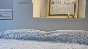 Een slaapkamer met een bed, voorzien van een wit- en blauw gebedrukte sprei, een keurig opgevouwen witte deken en een kunstwerk in een lijst erboven.