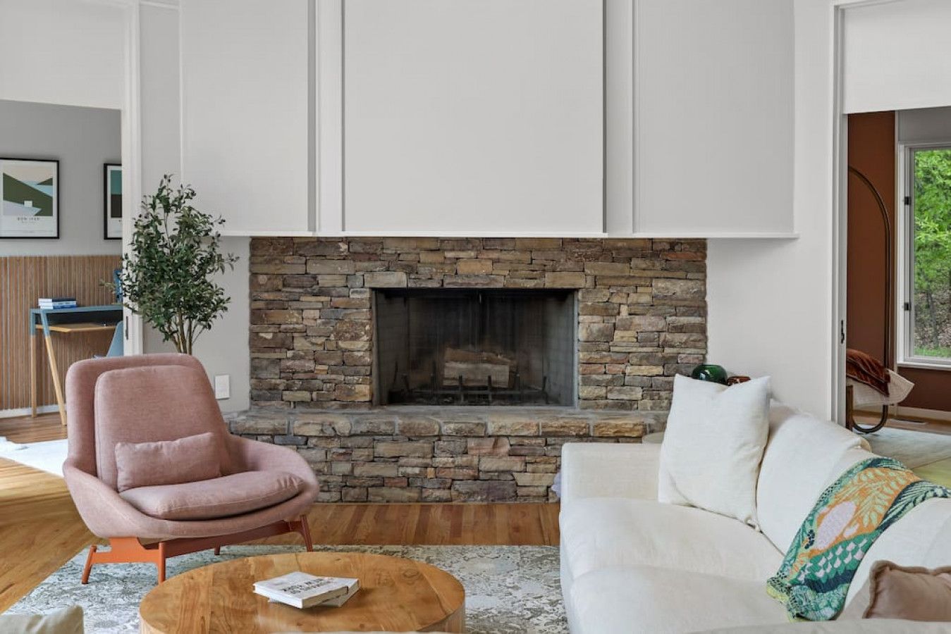 A modern living room with a stone fireplace, a pink armchair, a white sofa, and a wooden coffee table.
