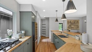 Eine moderne Küche mit grauen Schränken, einer Holzausziehtafel, einem Gasherd und Pendelleuchten.
