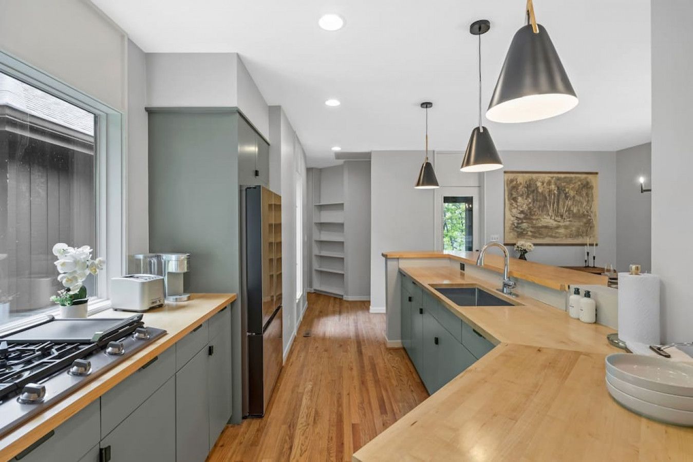 A modern kitchen with a central island, wooden flooring, and pendant lighting.