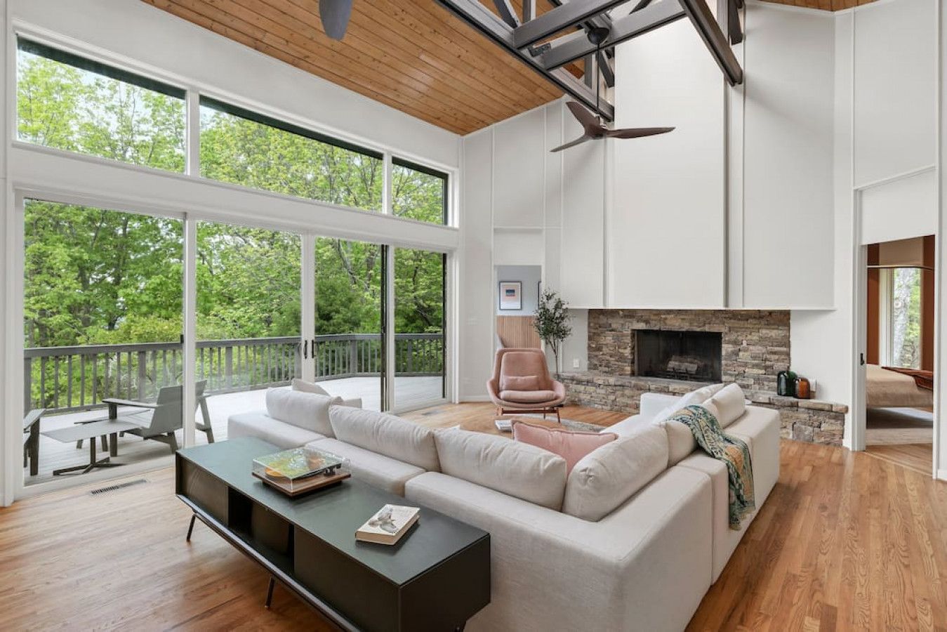 A spacious living room with a large sectional sofa, a fireplace, and a balcony with a view of trees.