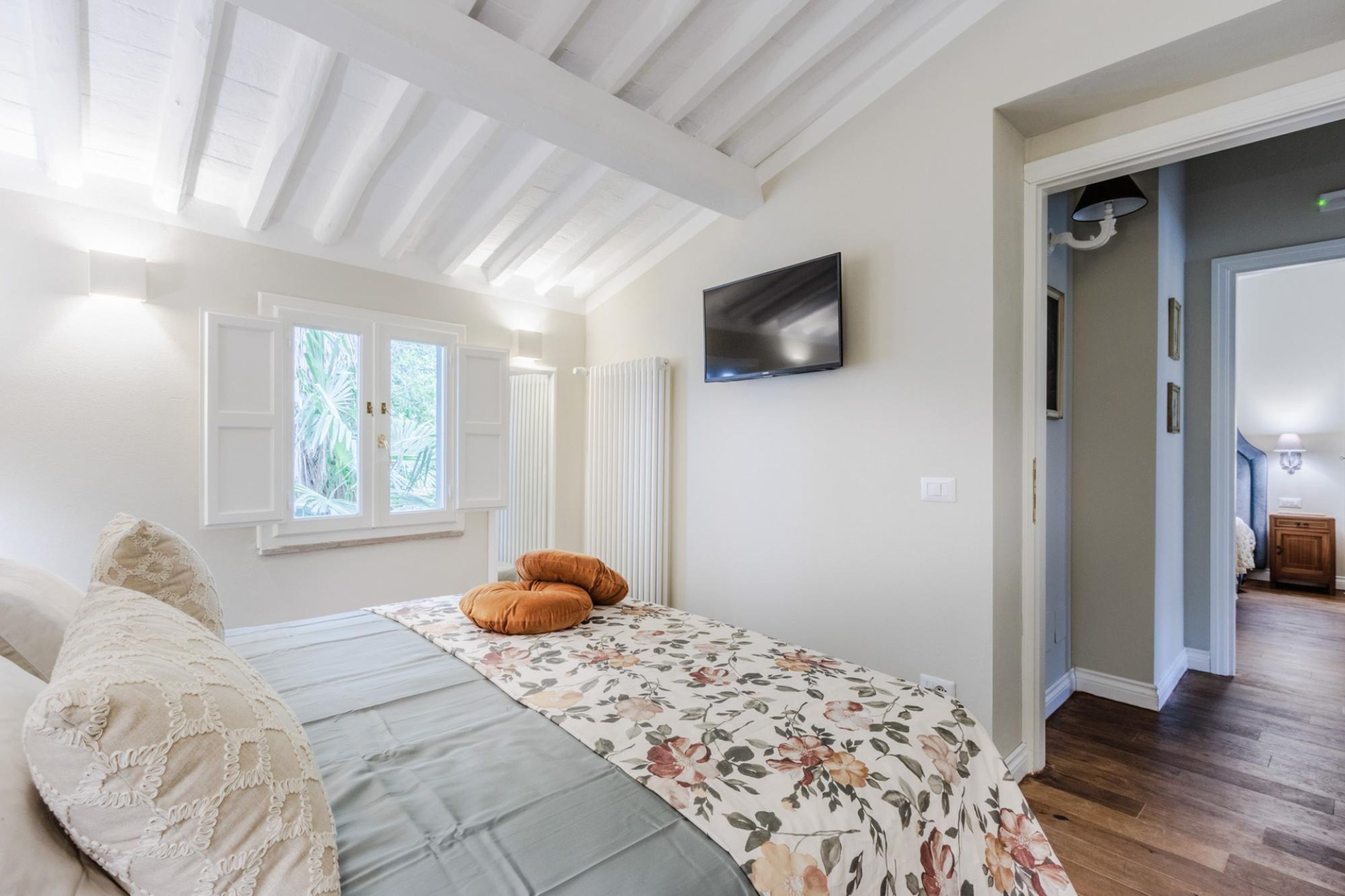 A bedroom with a bed, a TV mounted on the wall, and a window with shutters.