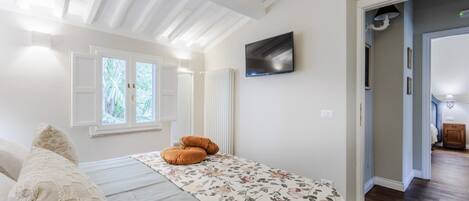 A bedroom with a bed, a TV mounted on the wall, and a window with shutters.