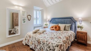 A bedroom with a floral bedspread, a large mirror, and a wooden nightstand with a lamp. - Casa Chiostro in Lucca (Lucca)
