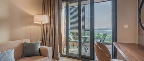 Una habitación de hotel moderna con sofá, escritorio y vistas al exterior a través de un ventanal corredero.