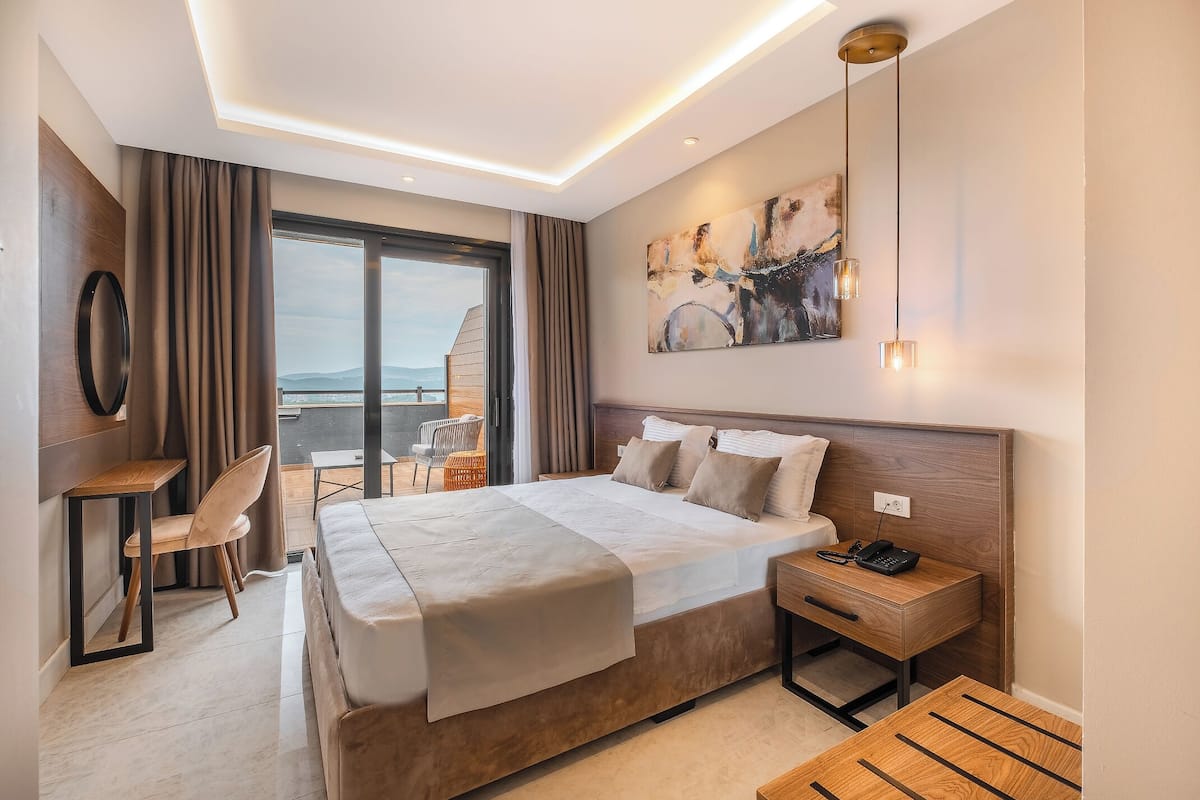 A modern hotel room with a large bed, a desk, and a view of the sea.