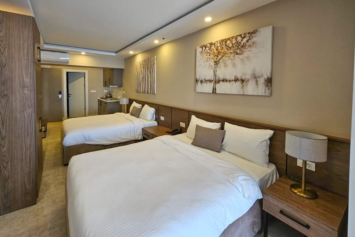 A hotel room with two beds, a small desk, a nightstand, a lamp, and a painting on the wall.