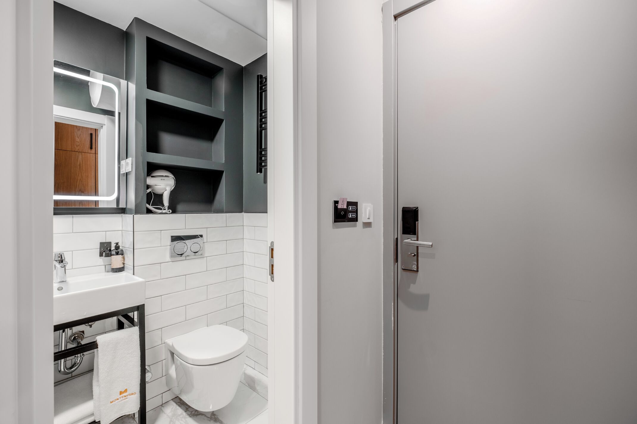 Une salle de bain moderne avec un lavabo blanc, des toilettes et un sèche-cheveux. On y trouve un porte-serviettes sur lequel est posée une serviette.