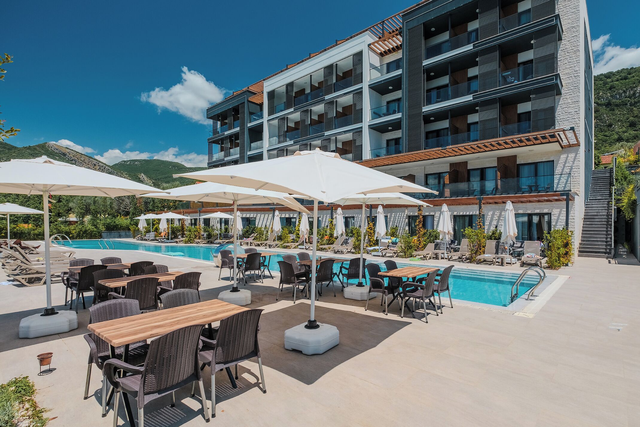 A hotel with a pool area, outdoor seating, and a multi-story building with balconies.