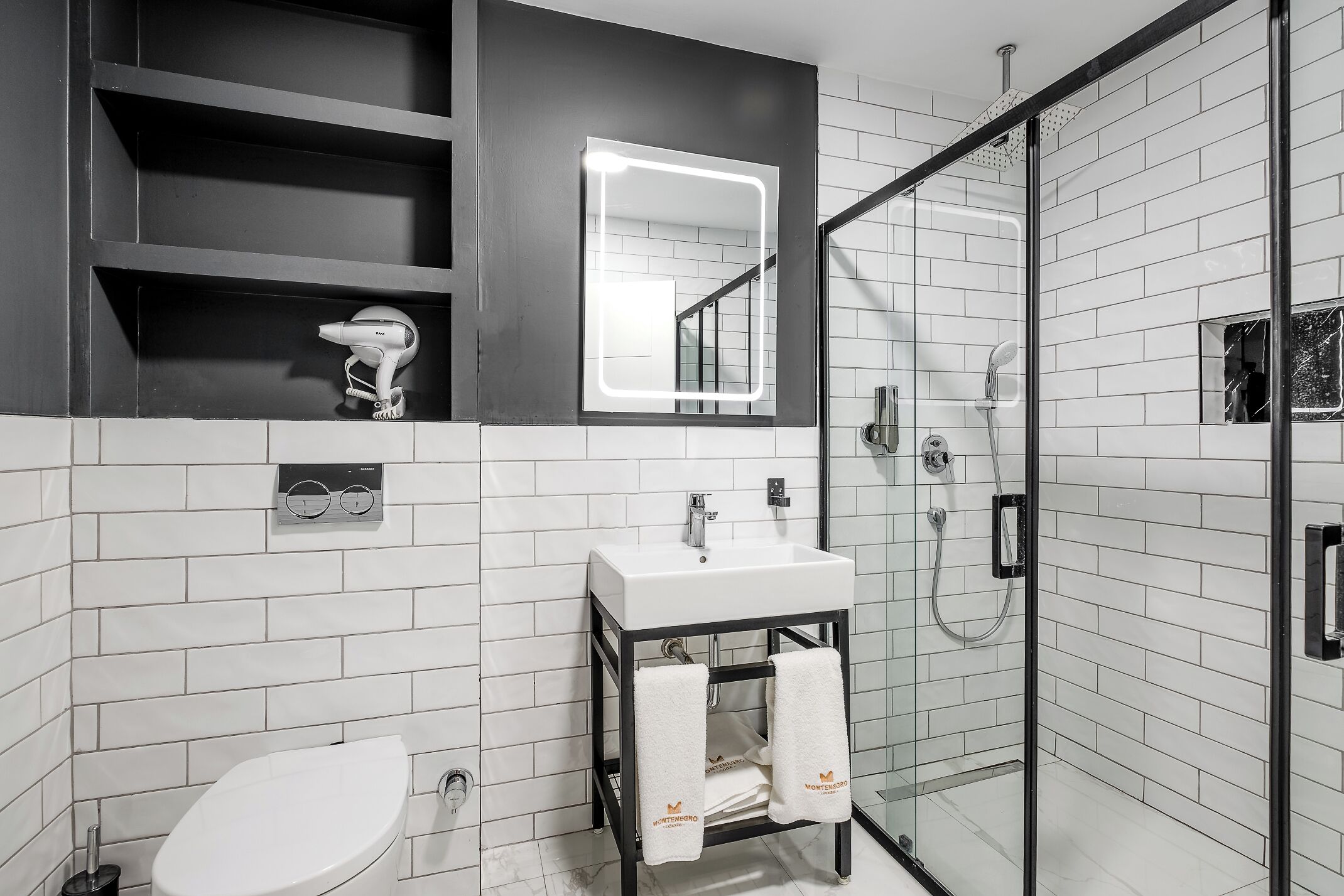 Une salle de bain moderne avec des toilettes blanches, un lavabo avec un miroir et une douche à parois de verre.