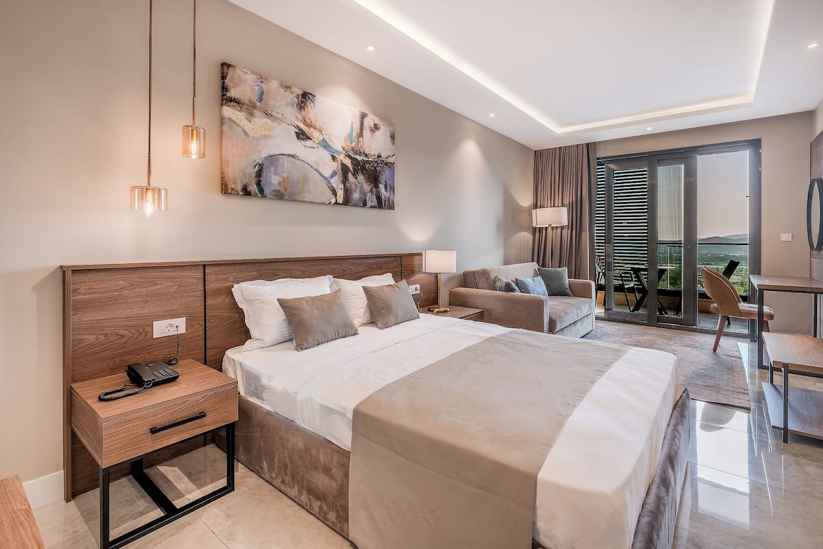 A modern hotel room with a large bed, a desk, and a balcony with a view.