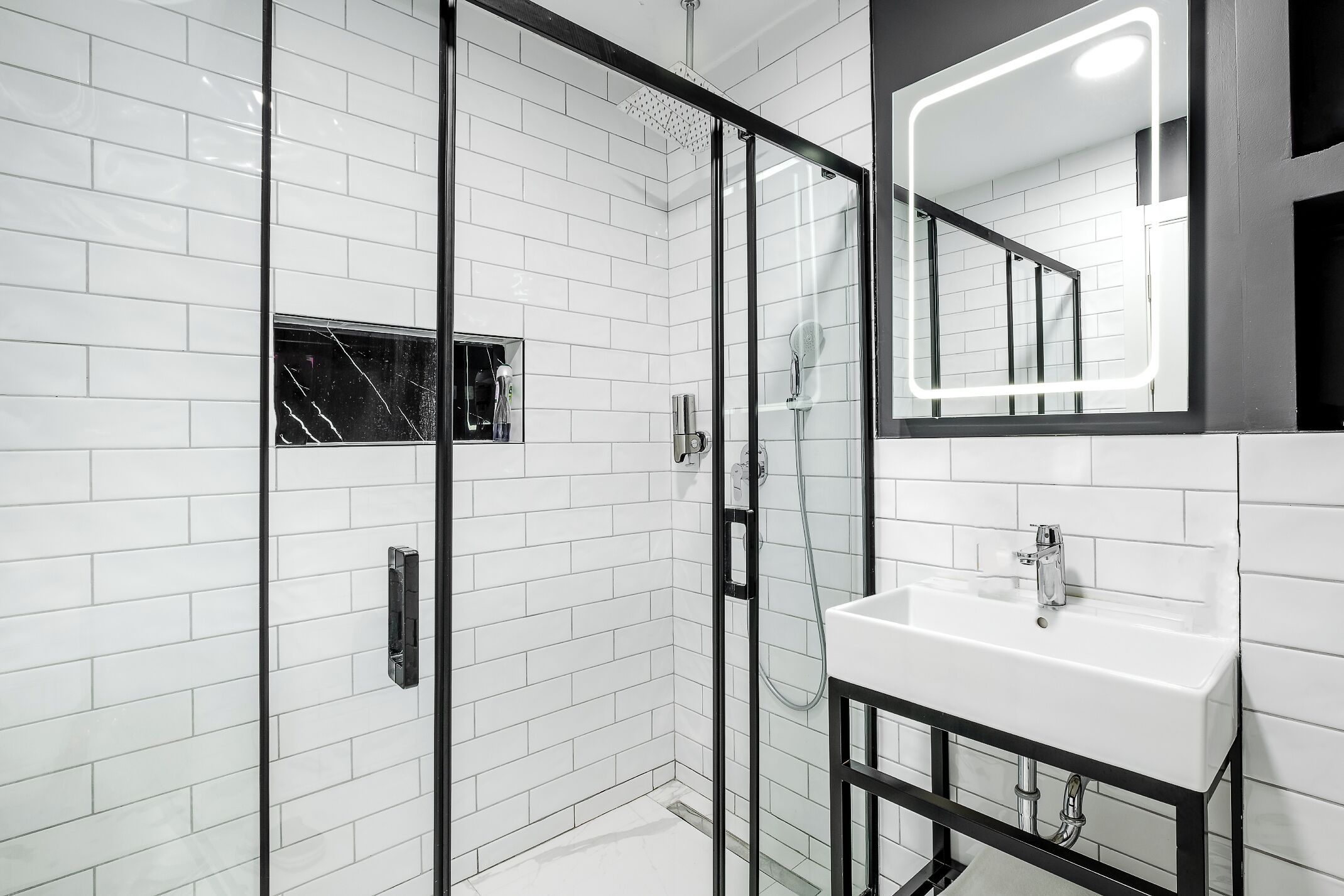 A modern bathroom with a glass-enclosed shower, a white sink, and a large mirror with a lighted frame.