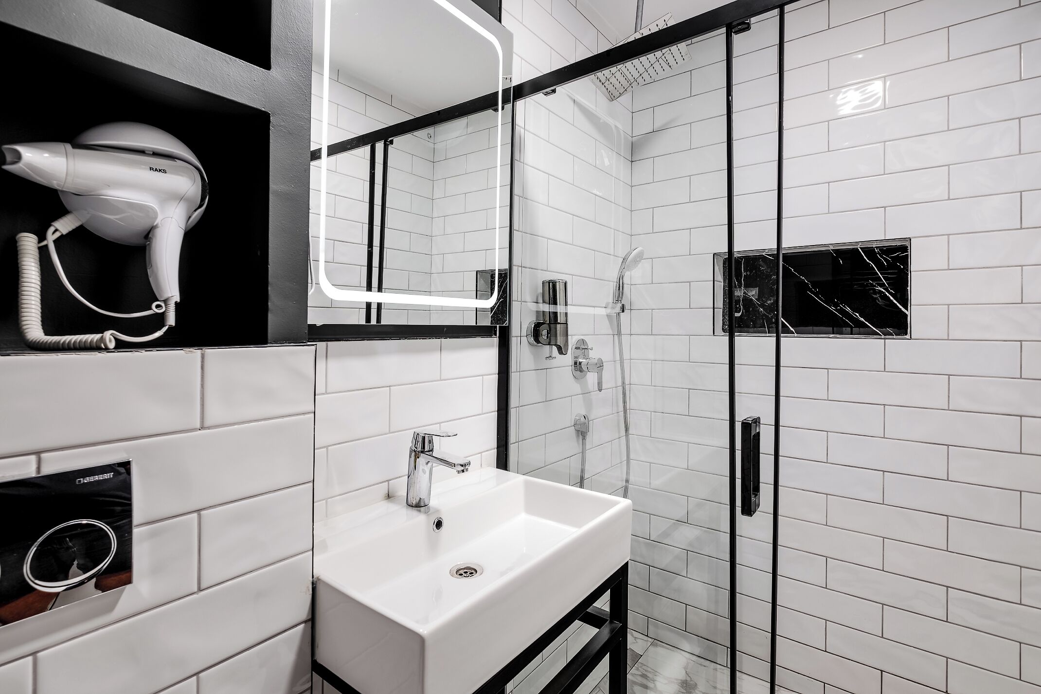 A modern bathroom with a white sink, a hairdryer, and a glass-enclosed shower.