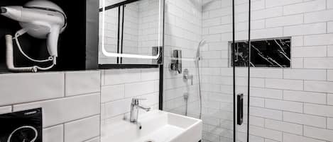 A modern bathroom with a white sink, a hairdryer, and a glass-enclosed shower.