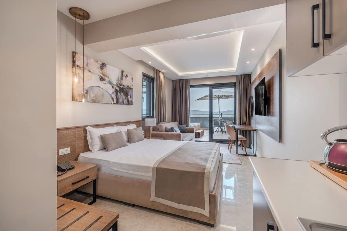 A modern hotel room with a large bed, a desk, a chair, and a balcony with a table and chairs.