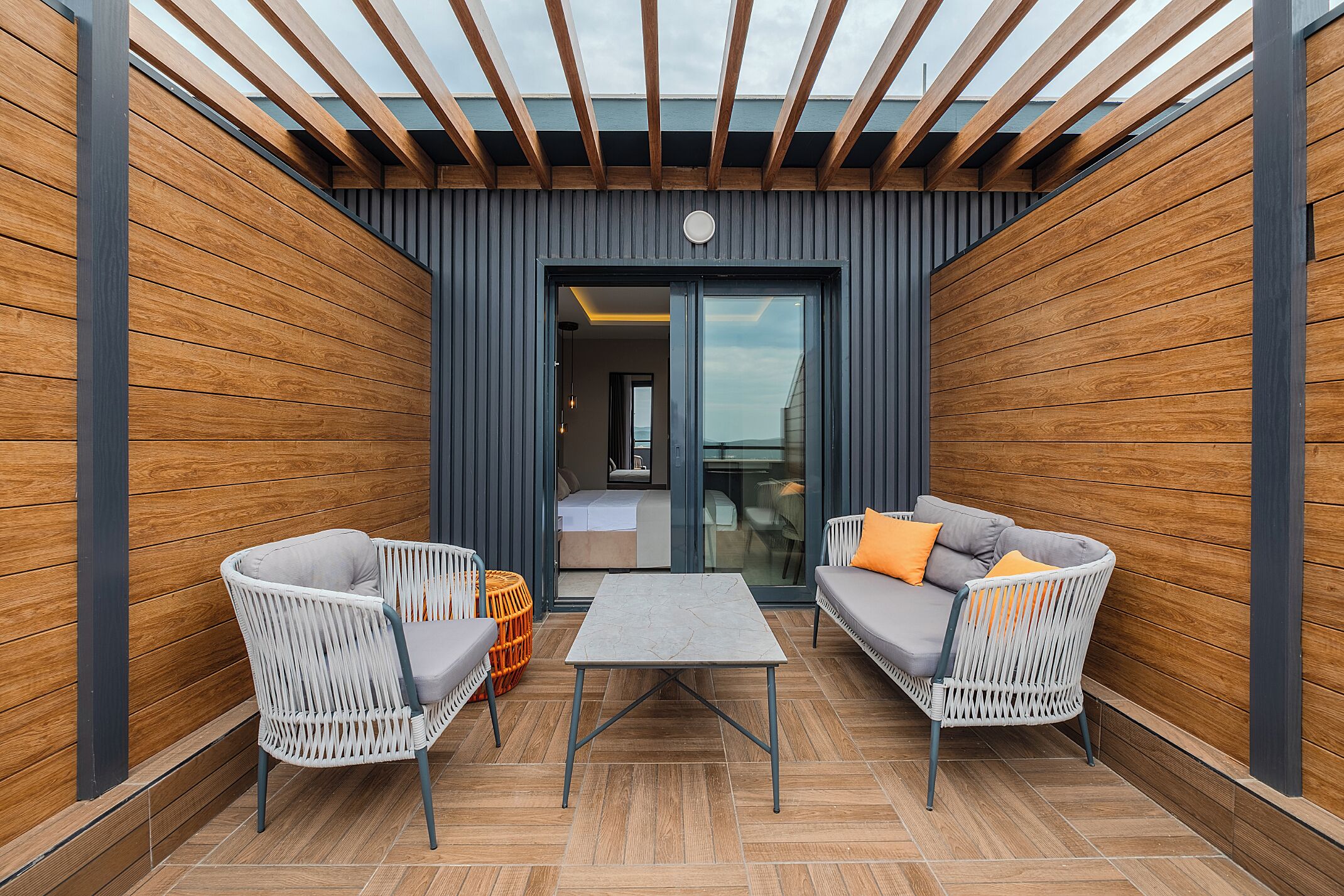 An outdoor patio with two wicker chairs, a small table, and a sofa with cushions.