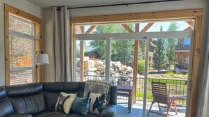A cozy living room with a black leather sofa, a coffee table, and a view of a wooden deck and outdoor area. - 2 Kg Beds+ Walk to Ponds, Pool, Hot tub&River. Short Drive to RMNP & Winter Park (Granby)
