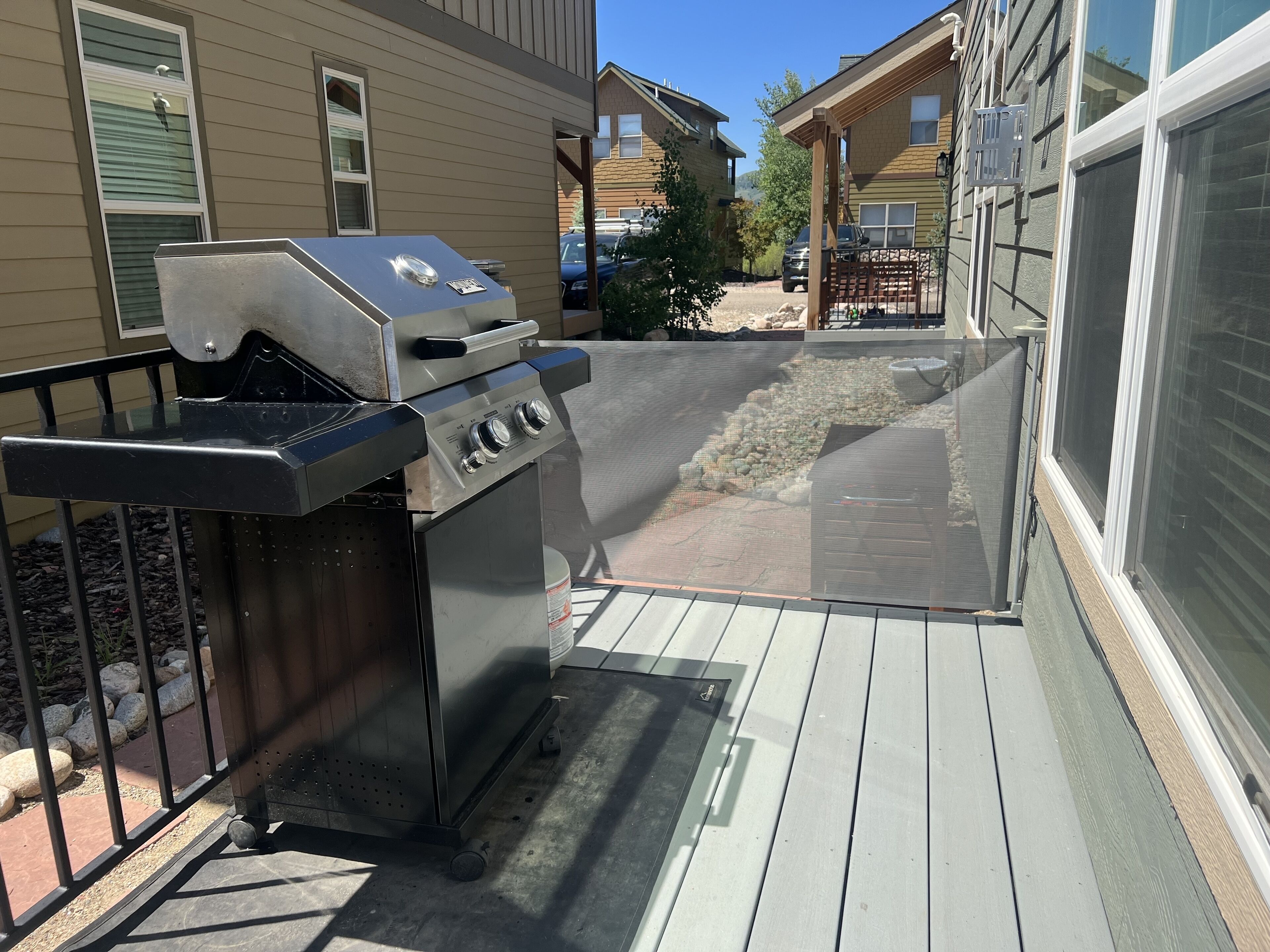 A barbecue grill on a deck with a view of neighboring houses.