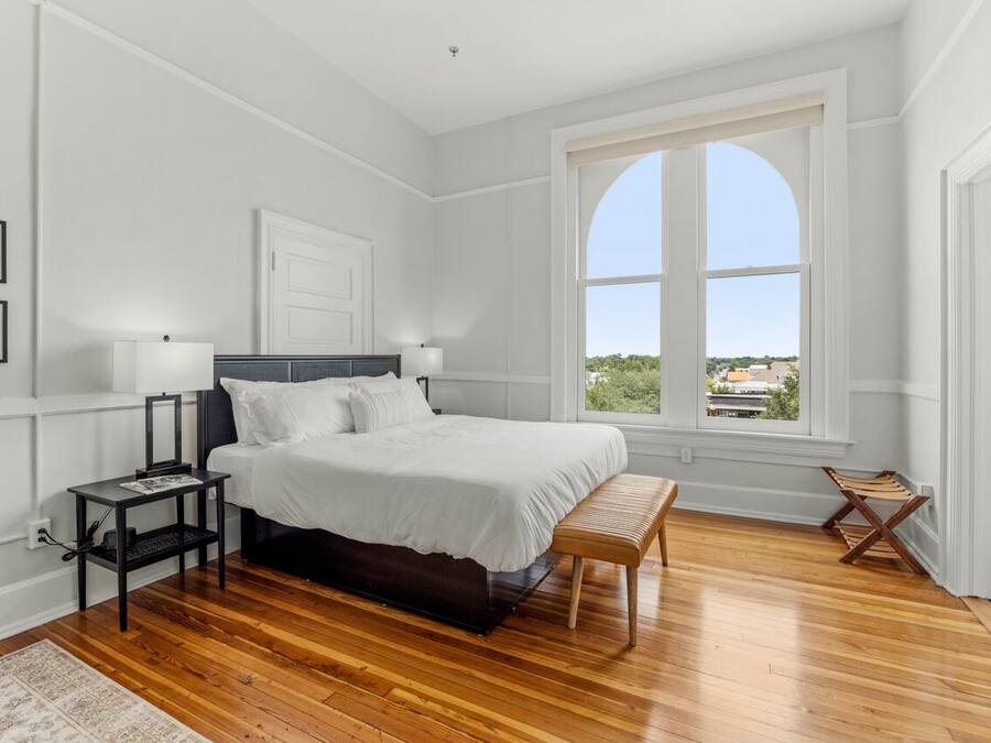 Een slaapkamer met een groot bed, een nachtkastje, een bankje en een raam met uitzicht.