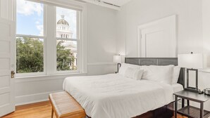 A bedroom with a large window, a bed, a nightstand, and a bench. - The McKey (Valdosta)
