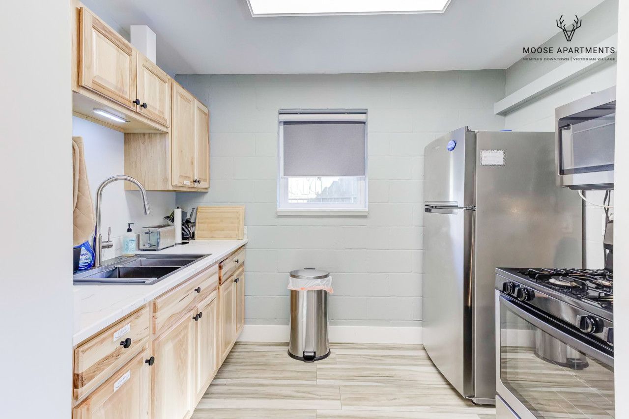 A modern kitchen with wooden cabinets, a stainless steel refrigerator, a stove, and a window with a blind.