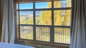 A bedroom with a large window, a bed, and a ceiling fan. - Cozy Cabin: Summer paradise on the river (Granby)