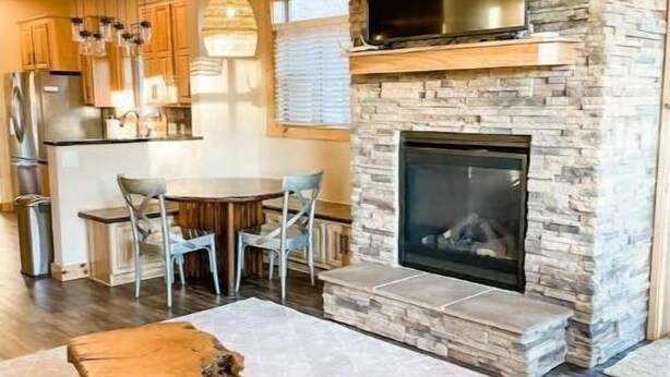 A modern kitchen with wooden cabinets, a built-in oven, and a dining area with a table and chairs. - Cozy Cabin: Summer paradise on the river (Granby)