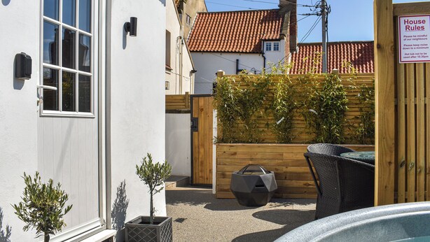 A white building with a wooden fence, a hot tub, and a sign indicating house rules.
