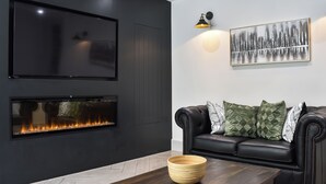 A modern living room with a black leather sofa, a flat-screen TV, a fireplace, and a decorative wall piece.