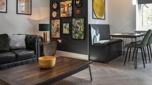 A modern living room with a dark wall, a wooden coffee table, a leather sofa, and a dining area with chairs and a table.