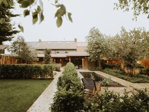 Une maison moderne avec un jardin, un banc en bois et un chemin menant à l’entrée.