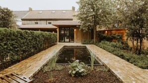 A courtyard with a rectangular water feature, a wooden bench, and a building with a tiled roof in the background. - Huyze Ter Bercken with swimming pond by Interhome (De Haan)