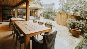 An outdoor dining area with a wooden table and chairs, surrounded by a wooden fence and potted plants. - Huyze Ter Bercken with swimming pond by Interhome (De Haan)