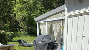 Una terraza de madera con una parrilla, mobiliario exterior y macetas.