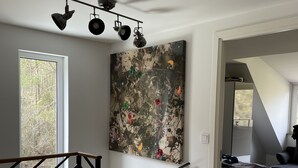 Un interior moderno con una escalera, un cuadro abstracto grande y vistas al exterior.