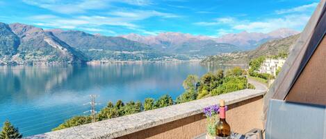 A terrace with a table set for two, overlooking a lake with mountains in the background.