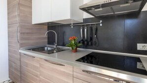 Une cuisine moderne dotée d’un évier en acier inoxydable, d’un four encastré et d’une hotte aspirante. On y trouve des armoires en bois et une petite plante en pot posée sur le plan de travail.