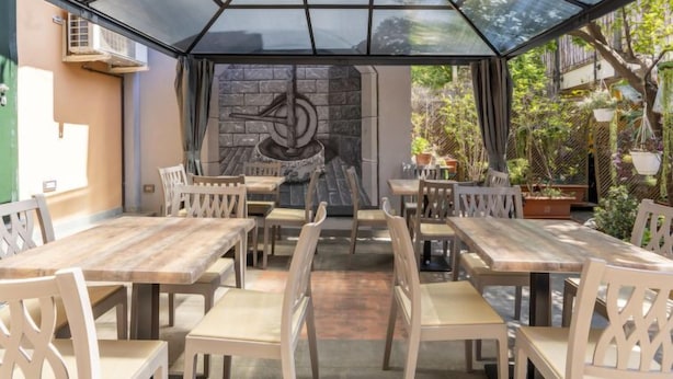 Une terrasse extérieure avec des tables et des chaises en bois, un toit en verre et un mur de pierre en arrière-plan.