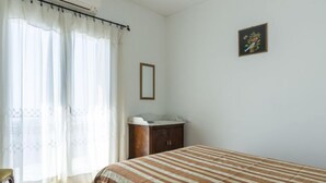 Une chambre à coucher avec un lit, une table de chevet, un miroir et une fenêtre avec des rideaux.