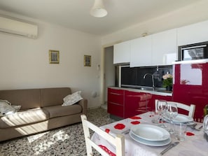 Een compacte leefruimte met een kitchenette, een eethoek voor twee personen en een bank.