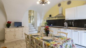 Een eetgedeelte met een tafel voor vier personen, een keuken met witte kasten en een trap naar een hoger gelegen verdieping.
