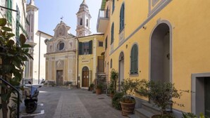 Une rue étroite bordée d’immeubles jaunes, une église avec un clocher et des plantes en pot le long du chemin.
