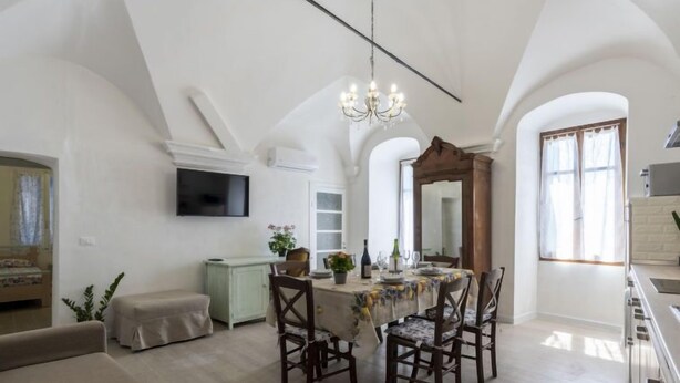 Un vaste espace dédié à la salle à manger, avec un plafond haut et un lustre, un téléviseur fixé au mur et un grand miroir au-dessus de la table à manger.