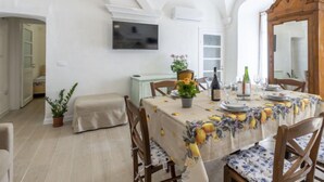 Un coin repas avec une table dressée pour quatre personnes, un lustre et un téléviseur fixé au mur.