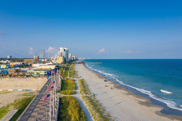 Un paysage urbain côtier avec une plage, une grande roue et une jetée qui s’avance dans l’océan.