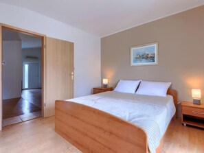 Ein Schlafzimmer mit einem hölzernen Bett, zwei Nachttischen mit Lampen, einem Bild an der Wand und einer Tür zu einem anderen Raum.
