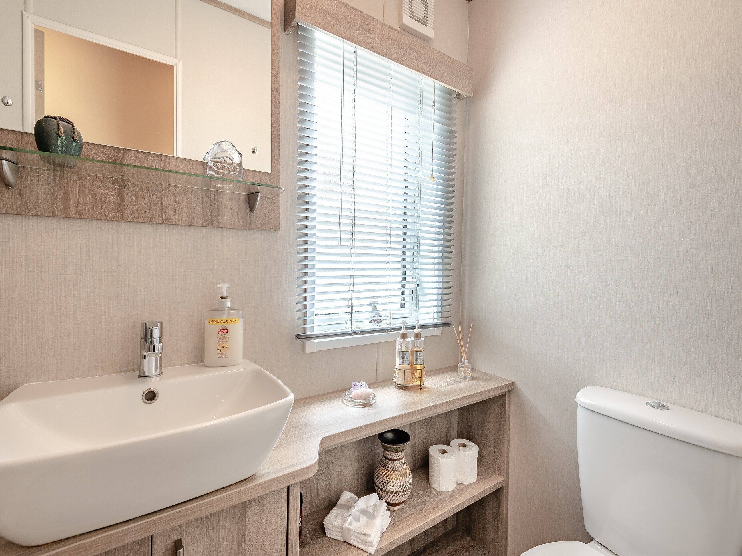 Une salle de bain avec un grand lavabo, un miroir, une fenêtre avec des stores et des toilettes.